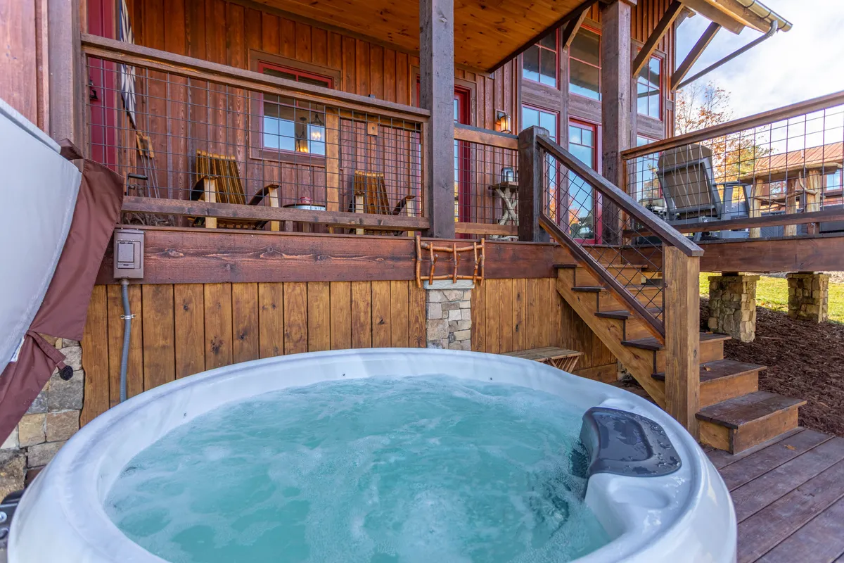 A serene exterior shot of a private wooden deck with a bubbling hot tub and a staircase leading down to more outdoor space. Surrounded by nature, the deck is ideal for evening relaxation after a day of resort activities.