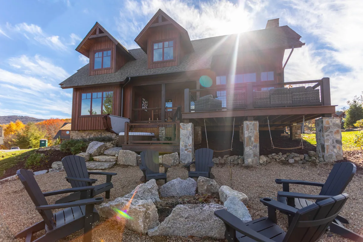 This image features the exterior of the house with a welcoming fire pit surrounded by Adirondack chairs, set against a backdrop of lush greenery. The arrangement invites groups to gather outdoors for conversation, storytelling, and relaxation.