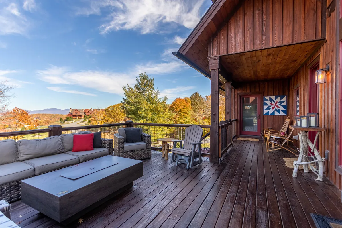 A spacious deck with comfortable seating and panoramic natural scenery, including distant mountains and lush greenery. A decorative quilt pattern adds a homey, inviting touch to the space.