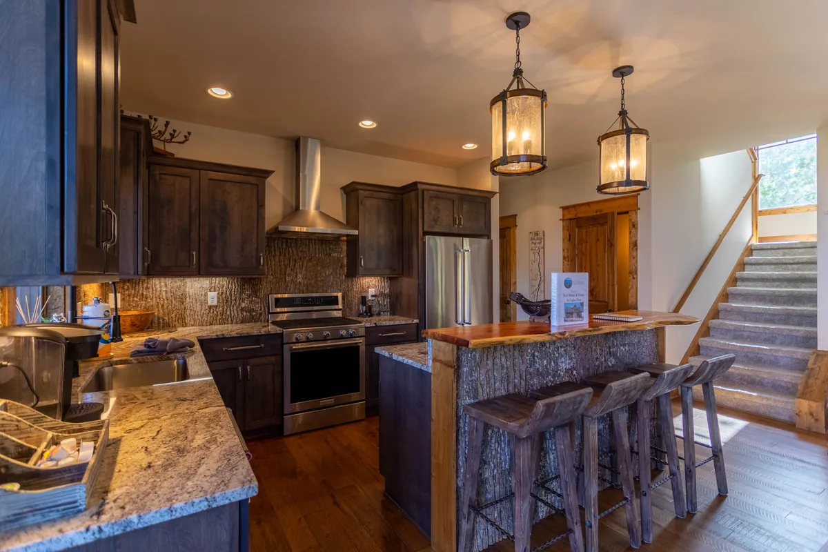 A bright, open kitchen with a spacious granite island surrounded by bar stools. Stainless steel appliances, pendant lighting, and plenty of counter space invite group cooking and socializing. The warm-toned cabinetry and décor create a stylish yet welcoming environment.