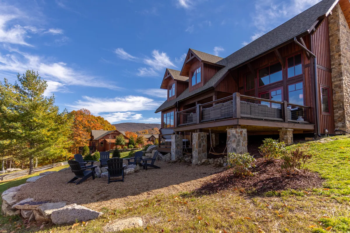 The image showcases the home's exterior with large windows and an inviting seating area, set within a picturesque landscape. The setting suggests opportunities for group relaxation, outdoor meals, or sunset toasts with sweeping mountain views.