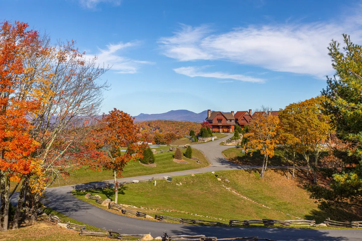 This exterior image captures the house with a winding road, vibrant trees, and mountains in the distance. The composition evokes a sense of adventure and the natural beauty of the surrounding Eagles Nest community, ideal for exploring and participating in nearby group activities.